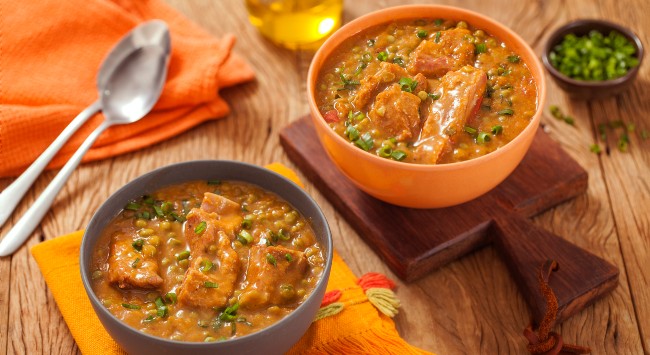 Dois bowls com sopa de ervilha e costelinha suina em cima de uma mesa com colher ao lado