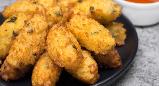 Bolinhos de arroz com carne moída servidos empilhados em um prato preto raso em uma mesa marmorizada cinza.