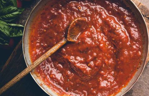 Panela de molho de tomate caseiro, com uma colher de pau dentro.