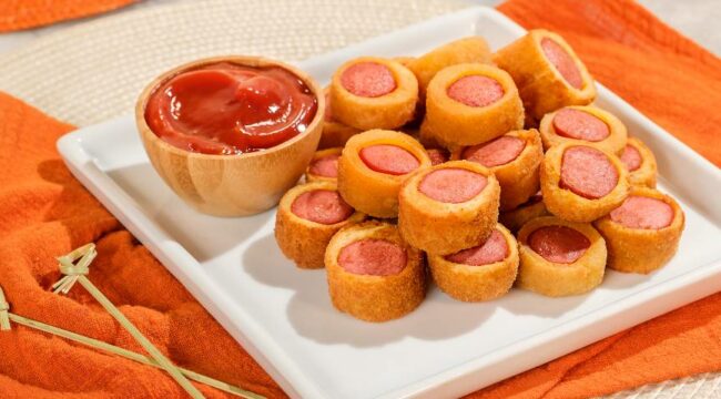 salgadinhos de salsicha servidos em prato branco acompanhados de ketchup