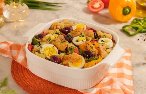 Bacalhau a portuguesa (com azeitonas roxas, ovo cozido, tomate cereja e coentro) servido em travessa branca.