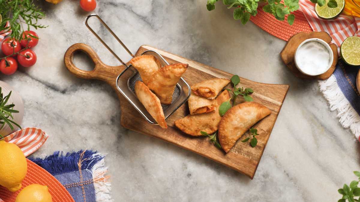 Imagem destaca uma porção de pastel de camarão frito servido em tábua de madeira com tigela de molho ranch ao lado.