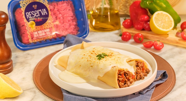 Panquecas de carne servida em um prato redondo ocm bordas mais elevadas. O prato esrá sobre um jogo americano marrom redondo e entre eles, um guardanapo azul. Ao fundo da imagem, do lado esquerdo, uma bandeja de Patinho Moído Reserva Friboi.